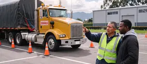 Instructor y alumno junto a un tractocamión con semirremolque en un patio de prácticas en Bogotá