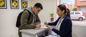 Alumno firma el formulario de matrícula en la recepción de la sede, atendido por una asesora